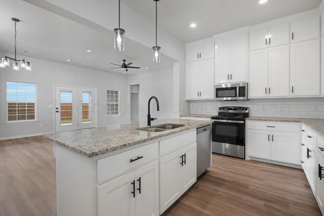 a kitchen with stainless steel appliances granite countertop a sink dishwasher a stove and a refrigerator with wooden floor