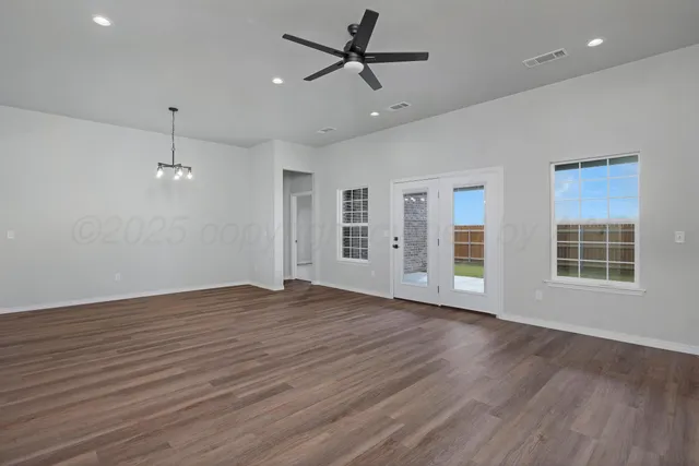 an empty room with wooden floor ceiling fan and windows