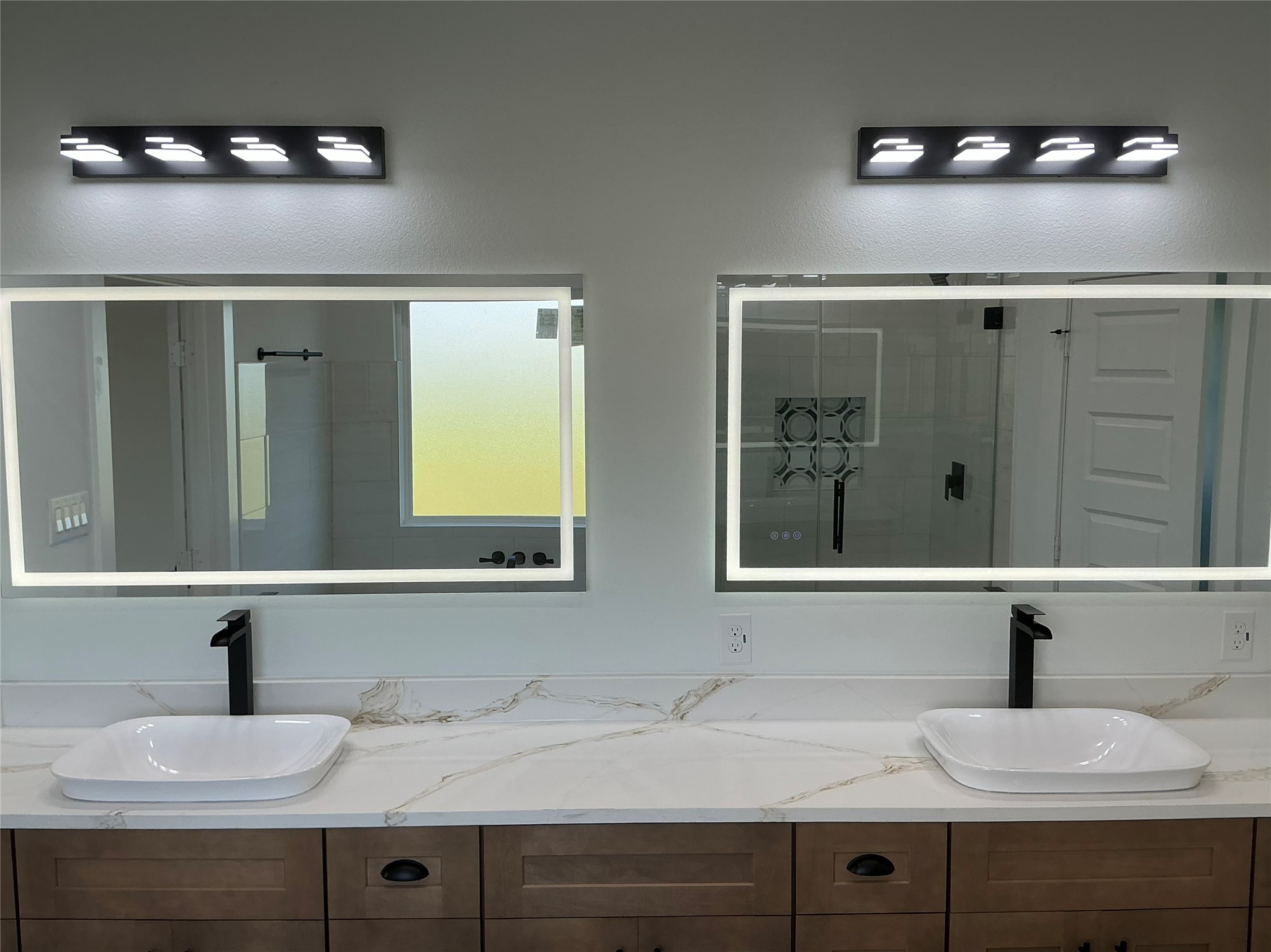 471 Buffalo Trail Angleton, TX 77515 - Photo 26 of 35 The master bathroom features a modern double vanity with sleek black fixtures, illuminated mirrors, and a quartz countertop. The space is well-lit with contemporary lighting and offers a clean, elegant design.