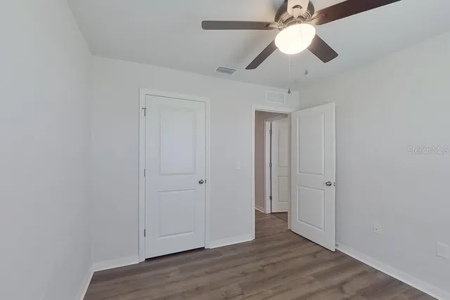 an empty room with wooden floor fan and windows