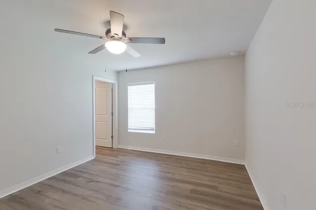 an empty room with wooden floor fan and windows