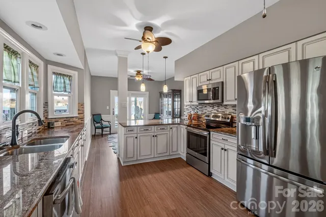 a kitchen with stainless steel appliances granite countertop a refrigerator a stove top oven a sink dishwasher and white cabinets with wooden floor