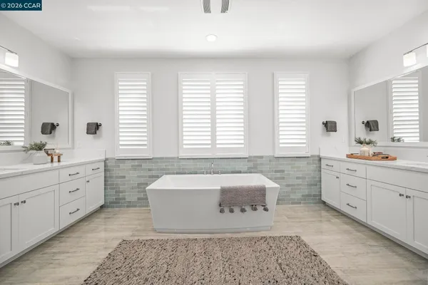 a spacious bathroom with double vanity a window a mirror a bathtub and window