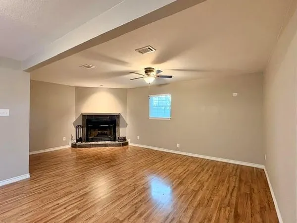 a view of an empty room with wooden floor fireplace and a window