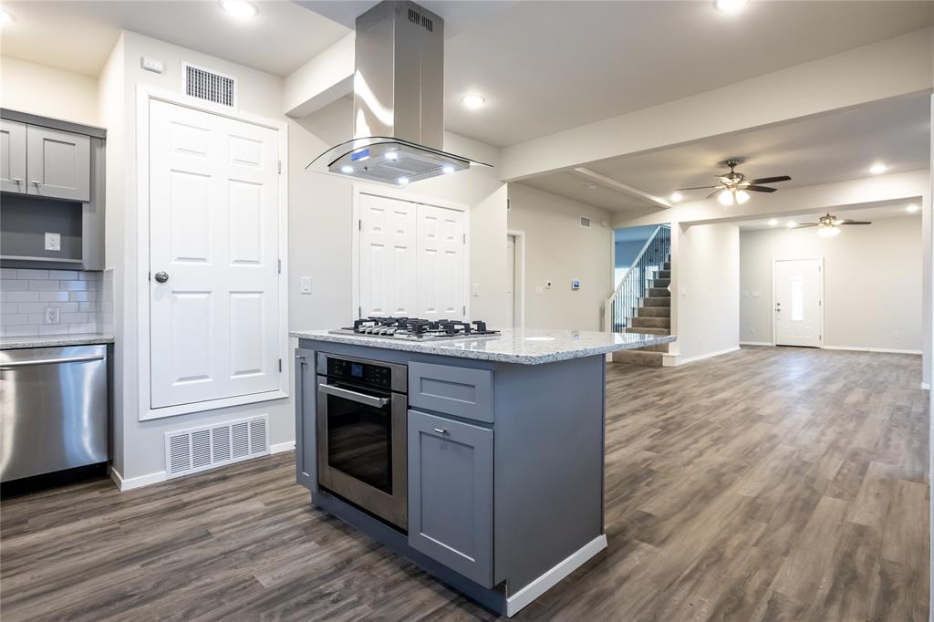 4522 Reiger Avenue Dallas, TX 75246 - Photo 9 of 37 Kitchen with island exhaust hood, light stone counters, stainless steel appliances, and dark hardwood / wood-style floors