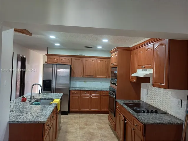 a kitchen with granite countertop kitchen island stainless steel appliances a sink stove and cabinets
