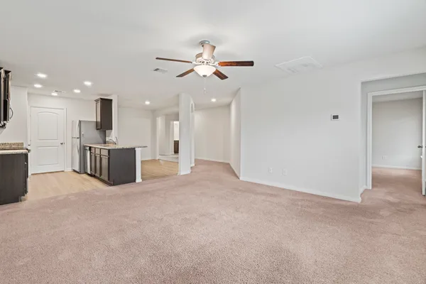 an empty room with kitchen view and a ceiling fan