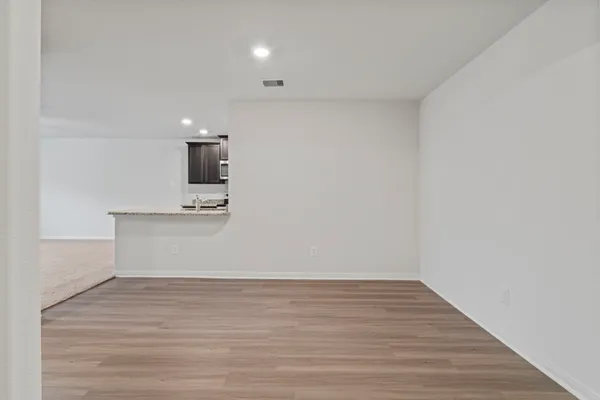 a view of kitchen and empty room with wooden floor