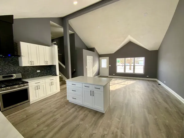 a large kitchen with kitchen island granite countertop a stove a sink a refrigerator and white cabinets with wooden floor