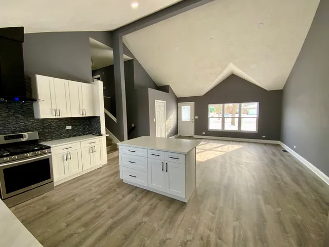 a large kitchen with kitchen island granite countertop a stove a sink a refrigerator and white cabinets with wooden floor