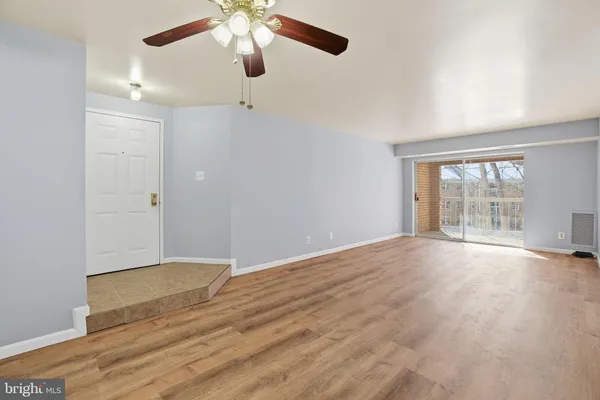 an empty room with wooden floor fan and windows