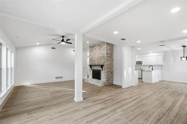 an empty room with wooden floor fireplace and windows
