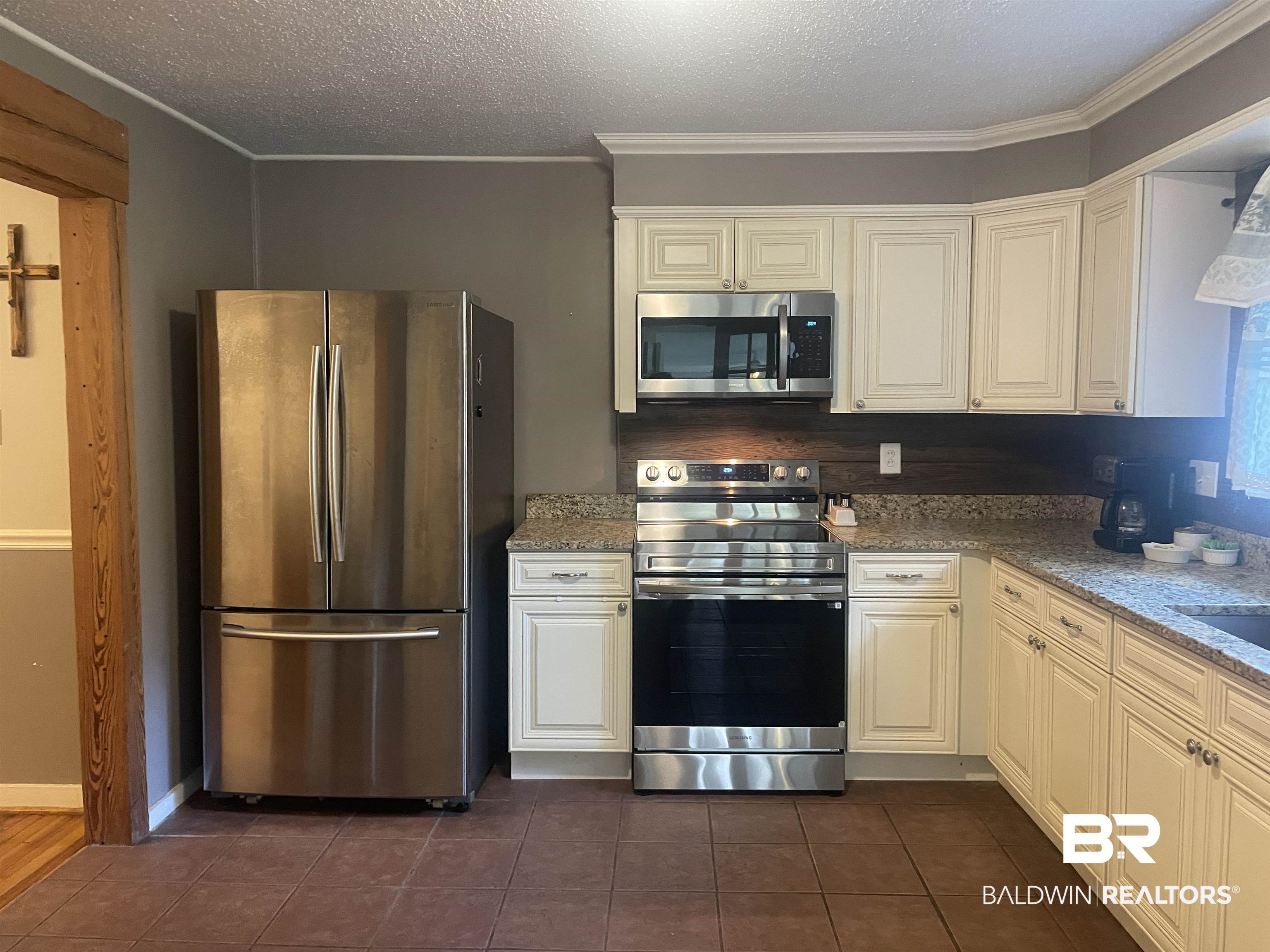 13850 Celeste Road Chunchula, AL 36521 - Photo 10 of 29 Kitchen featuring appliances with stainless steel finishes, ornamental molding, a textured ceiling, light stone counters, and dark tile patterned floors