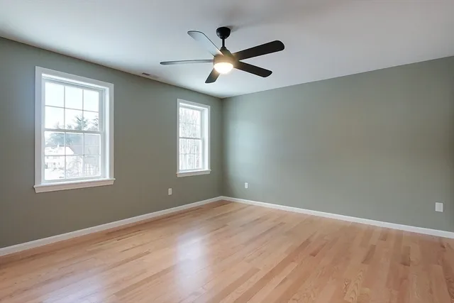 an empty room with wooden floor ceiling fan and windows