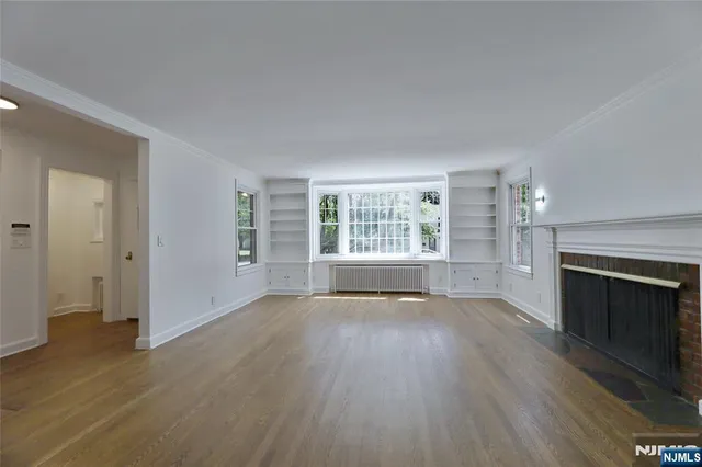 an empty room with wooden floor fireplace and windows