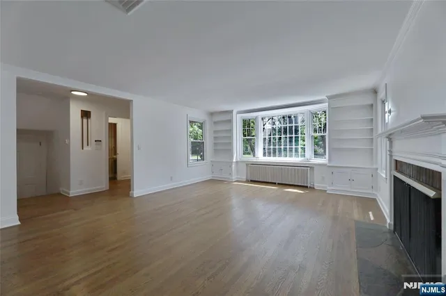 an empty room with wooden floor fireplace and windows