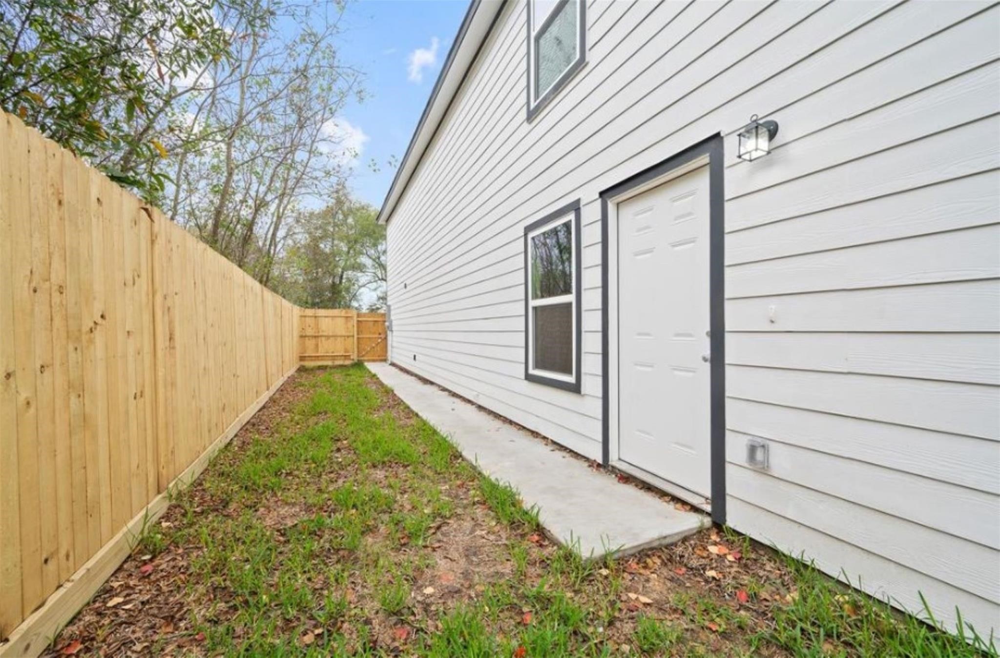 8120 Laura Koppe Road, Unit B Houston, TX 77028 - Photo 25 of 25 This photo shows a narrow side yard with a wooden fence, a concrete pathway, and the side of a white house with a door and windows.