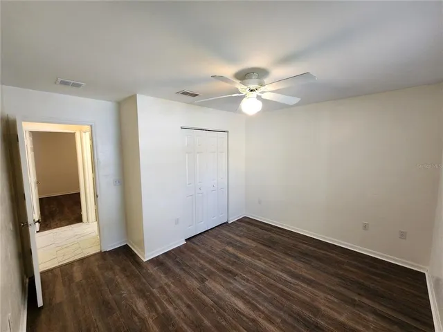 a view of an empty room with wooden floor and a ceiling fan
