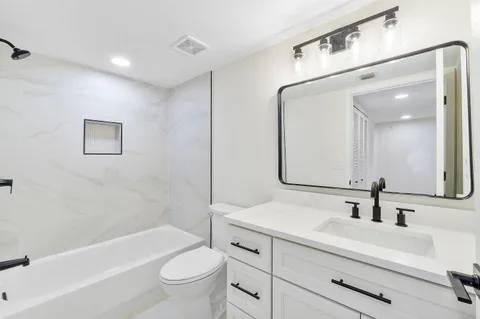 a bathroom with a bathtub shower sink vanity mirror and toilet