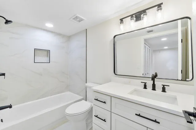 a bathroom with a bathtub shower sink vanity mirror and toilet