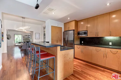 a kitchen with stainless steel appliances kitchen island granite countertop a refrigerator a stove a sink a dining table and chairs with wooden floor