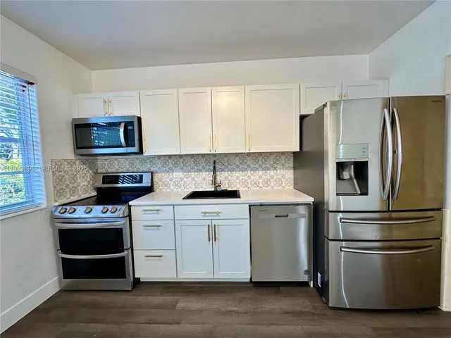 a kitchen with granite countertop stainless steel appliances a refrigerator cabinets and a window