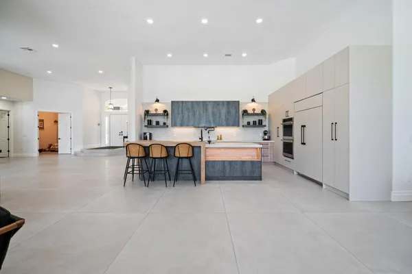 a large white kitchen with stainless steel appliances kitchen island granite countertop a refrigerator and a sink