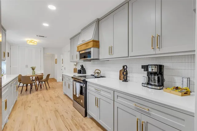 a kitchen with stainless steel appliances granite countertop a stove a sink and white cabinets with wooden floor