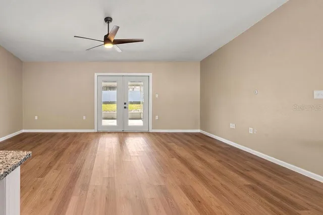 a view of an empty room with wooden floor ceiling fan and windows