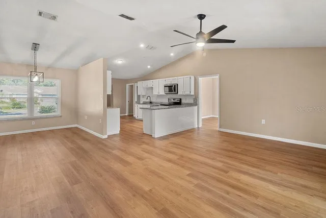 an empty room with wooden floor a ceiling fan and windows