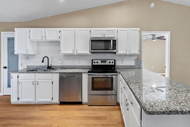 a kitchen with granite countertop a sink dishwasher a stove and a microwave oven with cabinets