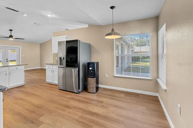 a large kitchen with stainless steel appliances a refrigerator a sink dishwasher a oven and white cabinets with wooden floor