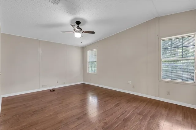 an empty room with wooden floor ceiling fan and windows