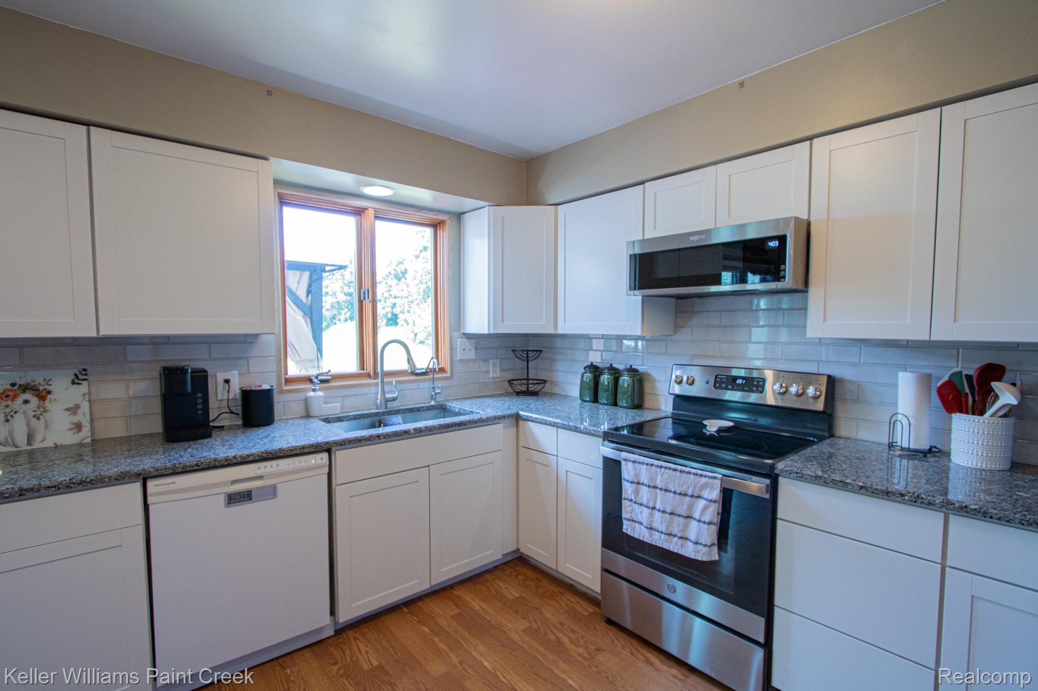 625 Howell Road Allenton, MI 48002 - Photo 13 of 46 White cabinetry, stainless steel appliances, wood-finish flooring, light-toned backsplash, and a window above the sink