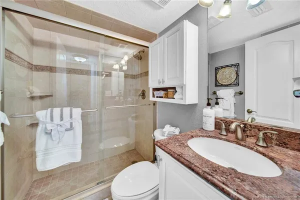 a bathroom with a granite countertop sink a toilet a mirror and shower