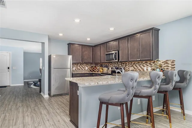 a kitchen with stainless steel appliances granite countertop a table chairs refrigerator and wooden floor