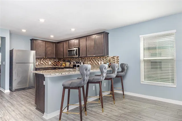 a kitchen with granite countertop a refrigerator a stove a sink and white cabinets with wooden floor