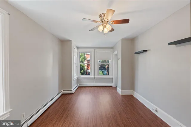 an empty room with wooden floor chandelier fan and windows