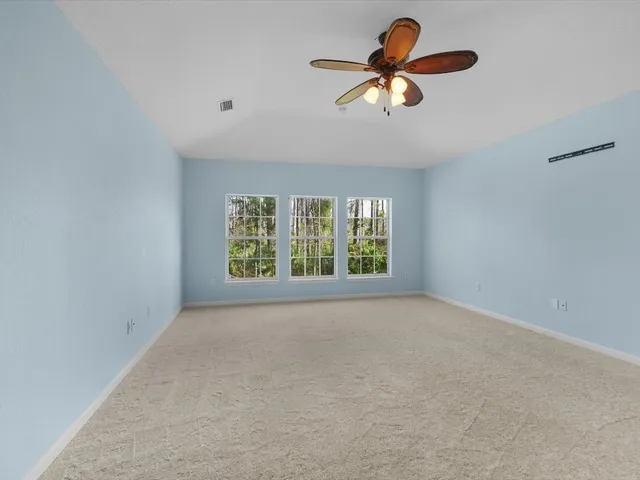 an empty room with chandelier fan and windows