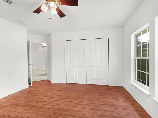 an empty room with wooden floor chandelier fan and windows