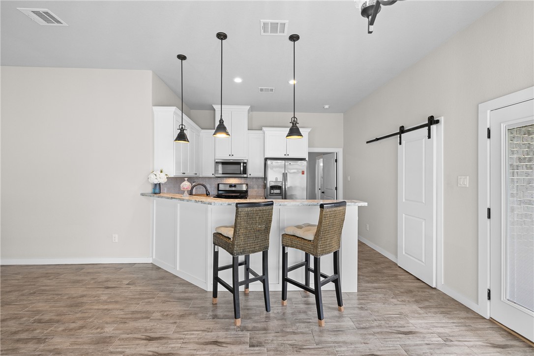 3088 Peterson Circle Bryan, TX 77802 - Photo 10 of 29 Kitchen featuring a barn door, a kitchen bar, a peninsula, tasteful backsplash, and appliances with stainless steel finishes