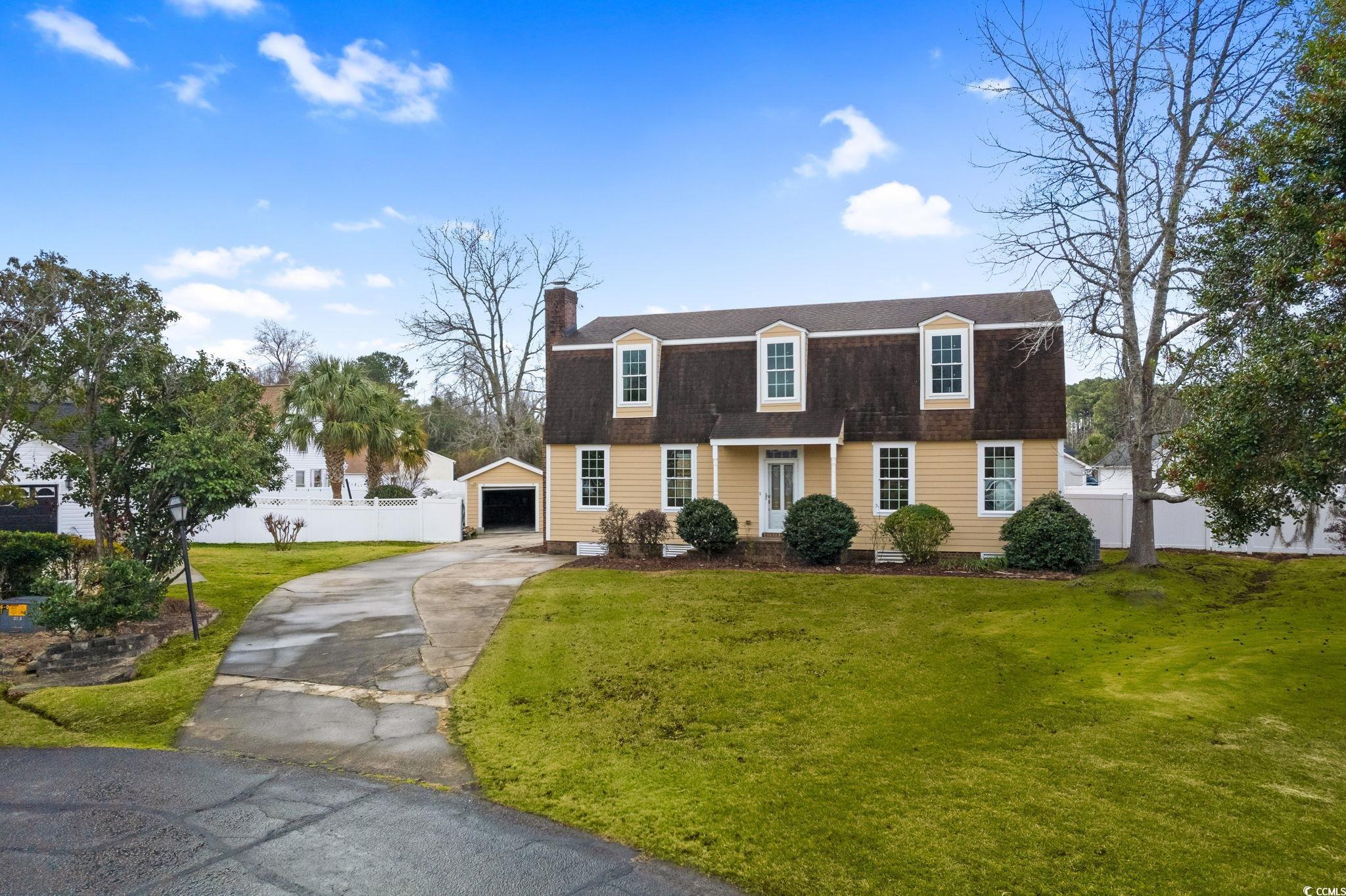 Colonial inspired home featuring a gambrel roof, roof with shingles, a chimney, concrete driveway, and a garage
