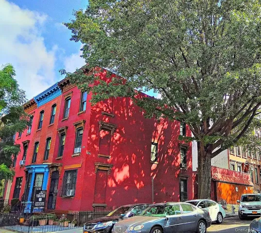 a front view of building with lot of trees and cars parked