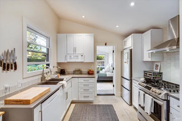 a kitchen with stainless steel appliances granite countertop a stove top oven a sink a refrigerator white cabinets and wooden floor