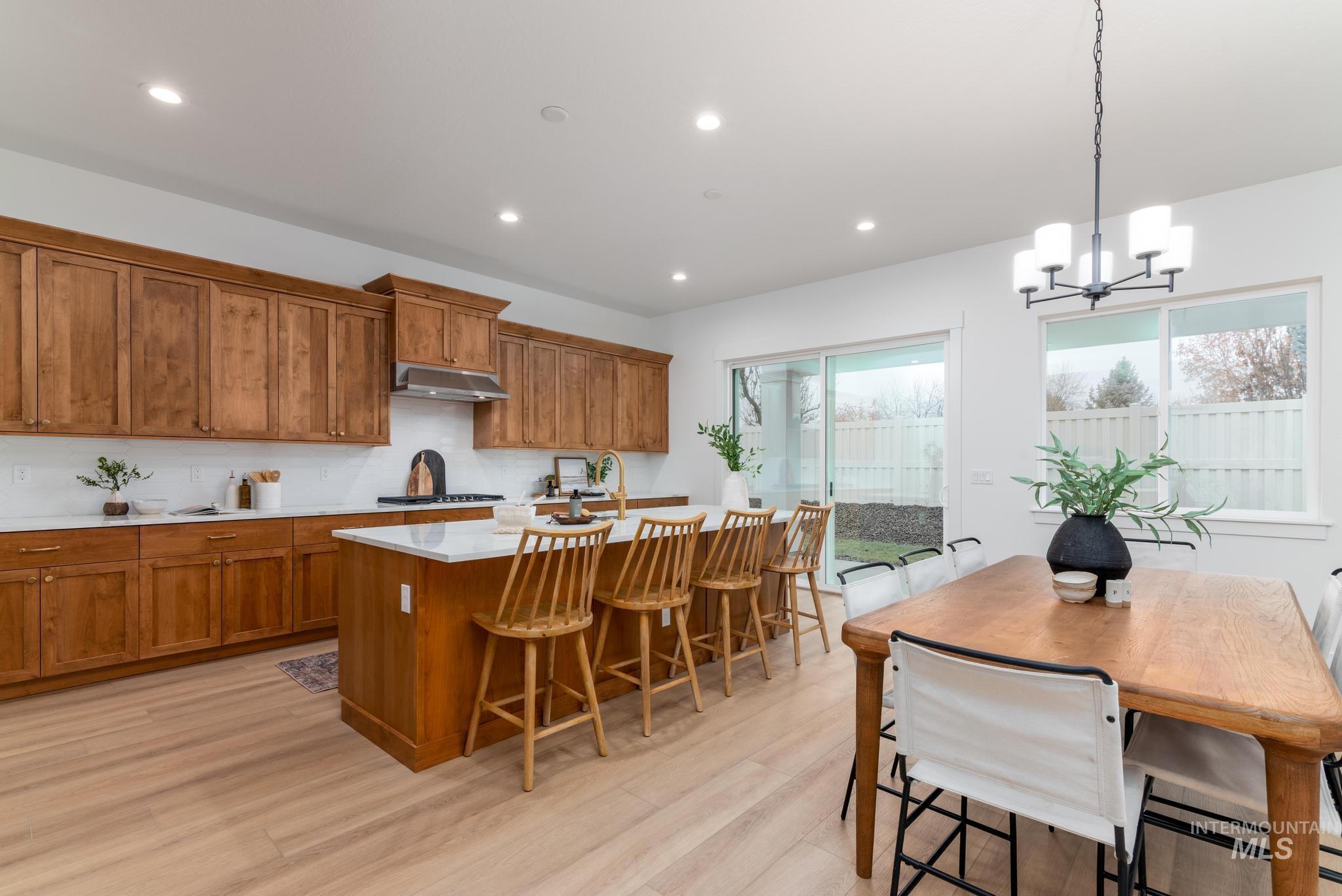 9044 West Purple Martin Street Star, ID 83669 - Photo 5 of 14 Kitchen with wood finish cabinetry, a center island with sink, light wood-style flooring, suspended lighting, and light stone counters