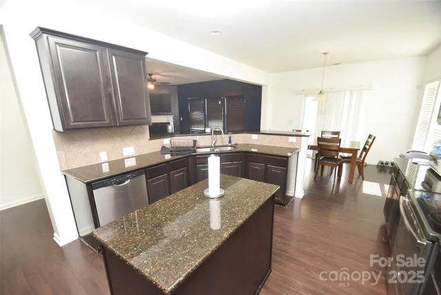 a kitchen with stainless steel appliances granite countertop wooden cabinets a sink a stove a dining table and chairs