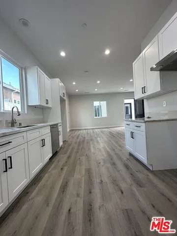 a kitchen with stainless steel appliances granite countertop a sink dishwasher a refrigerator and white cabinets with wooden floor