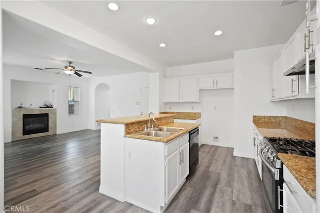 a kitchen with stainless steel appliances granite countertop a sink stove and white cabinets with wooden floor