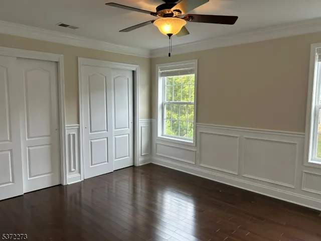 an empty room with wooden floor closet fan and windows