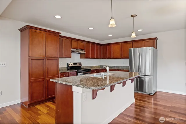 a kitchen with stainless steel appliances granite countertop a refrigerator a sink and a stove with wooden floors